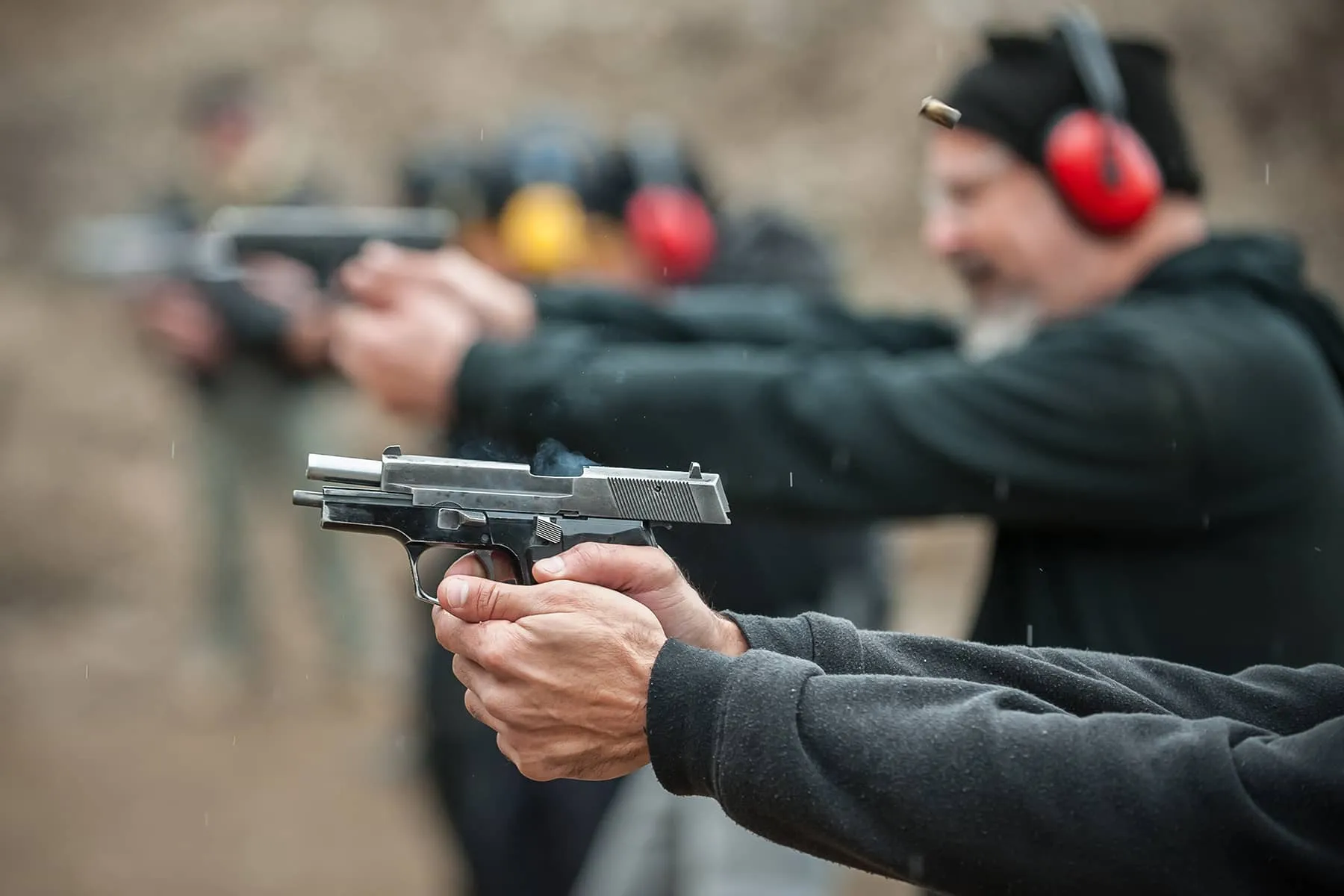 A group of people firing pistols in a open range